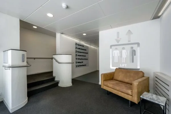 Wachtruimte bij lift op Van Leijenberghlaan met bruine bank, marmeren bijzettafel en trap naar kantoren.